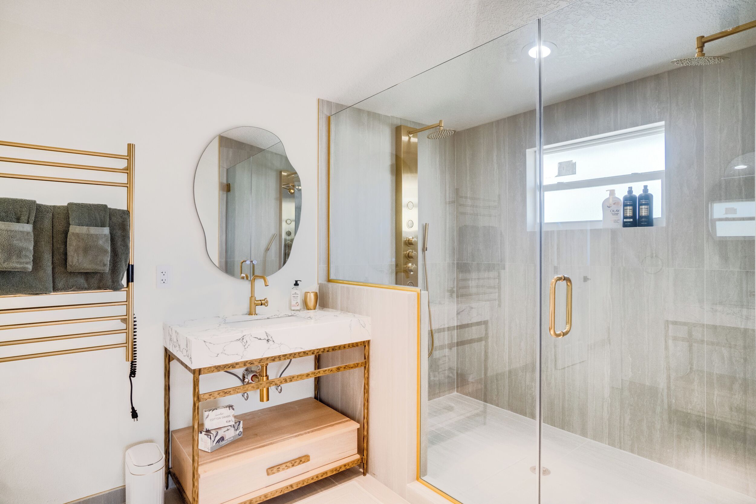 A modern bathroom with a glass-enclosed shower, a marble sink, and a gold-framed vanity.