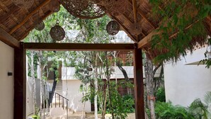 Un espacio al aire libre techado con un sendero de piedra, lámparas de mimbre colgantes y una escalera que lleva a un edificio.