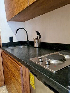 A kitchen with a black countertop, stainless steel stove, and wooden cabinets. - Jungle View Studio S11 Private Jacuzzi Pool (Tulum)