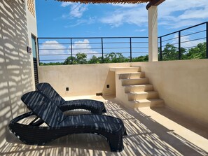 Varanda com cadeira, escadas e vista para árvores e céu.