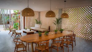 A spacious room with a large wooden dining table surrounded by chairs, a sofa, and hanging wicker lamps. - Jungle Escape Studio Quiet Cozy Gym Pool C5 (Tulum)