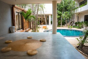 Ein moderner Poolbereich im Freien mit einer Betonplattform, einer großen Gewebematte und mehreren kleinen Hockstühlen.