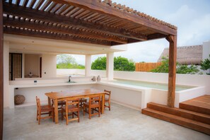 Ein Außenbereich mit Küche, der einen Holztisch, Stühle, eine integrierte Spüle und eine Pergola umfasst.