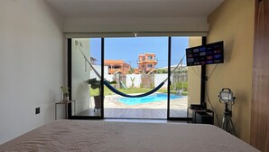 Una camera da letto con un letto grande, una TV a parete e vista su una piscina e edifici esterni.