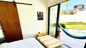 Camera da letto con un letto grande, un ventilatore a soffitto e vista su una piscina e sul verde circostante.