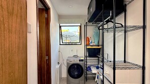 Una lavanderia con lavatrice, scaffali e una porta.