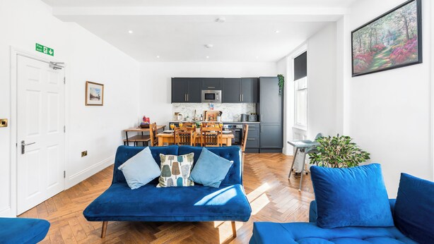 Una sala de estar moderna con un sofá azul, un comedor y una cocina al fondo.