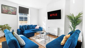 Una sala moderna con un sofá azul, una mesa de centro y una pantalla grande mostrando 'NETFLIX'.