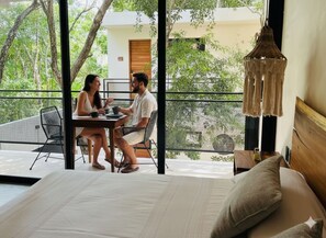 Een balkon met een eettafel en stoelen, een bed met hoofdeinde, en een hangende lamp.
