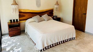 Een keurig opgemaakt slaapkamer met een groot bed, twee nachtkastjes en twee wandlampen van macramé.