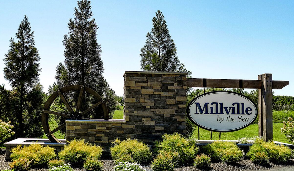 Une enseigne pour « Milville-sur-Mer », avec une structure en pierre et en bois, entourée de verdure et d’arbres.