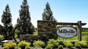 A sign for 'Milville by the Sea' with a stone and wooden structure, surrounded by greenery and trees.