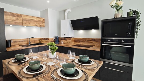 Een moderne keuken met een houten tafel voor vier personen, een inbouwoven en een tv aan de muur.
