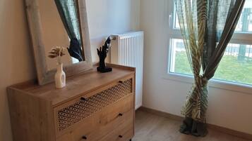 Een kamer met een houten dressoir, een spiegel, een vaas met bloemen en een raam met gordijnen.