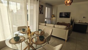Een moderne woonkamer met een glazen eettafel voor vier personen, een bank, een televisie en een lamp.