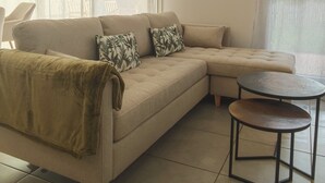Een woonkamer met een beige hoekbank, een kleine ronde tafel en een schilderij aan de muur.