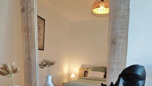 Een houten dressoir met een spiegel, een zwart buste beeldhouwwerk, en twee witte vazen met gedroogde bloemen.