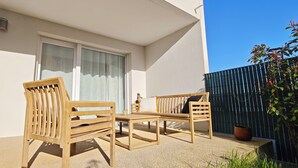 Een houten bank en tafelset op een balkon, met een raam en een bloempot.