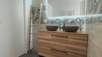 Ein Badezimmer mit zwei Waschbecken, einem Holzkosmetikschrank, einer Bambusleiter und gemusterten Fliesen.