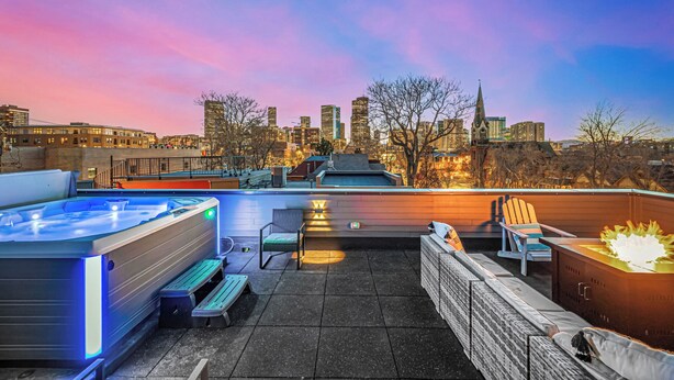 Eine Dachterrasse mit Whirlpool, Sitzgelegenheiten und Blick auf die Stadt im Abenddämmerung.