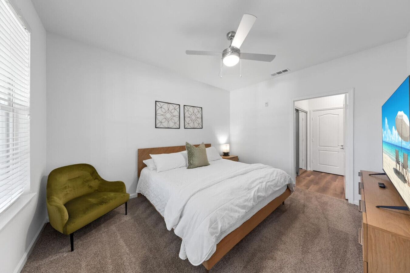 A bedroom with a bed, a green armchair, a ceiling fan, and a painting on the wall.