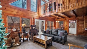 Ein gemütliches Blockhaus-Interieur mit Holzausstattung, einer großen Bärenstatue, einem Ledersofa und einem Weihnachtsbaum.