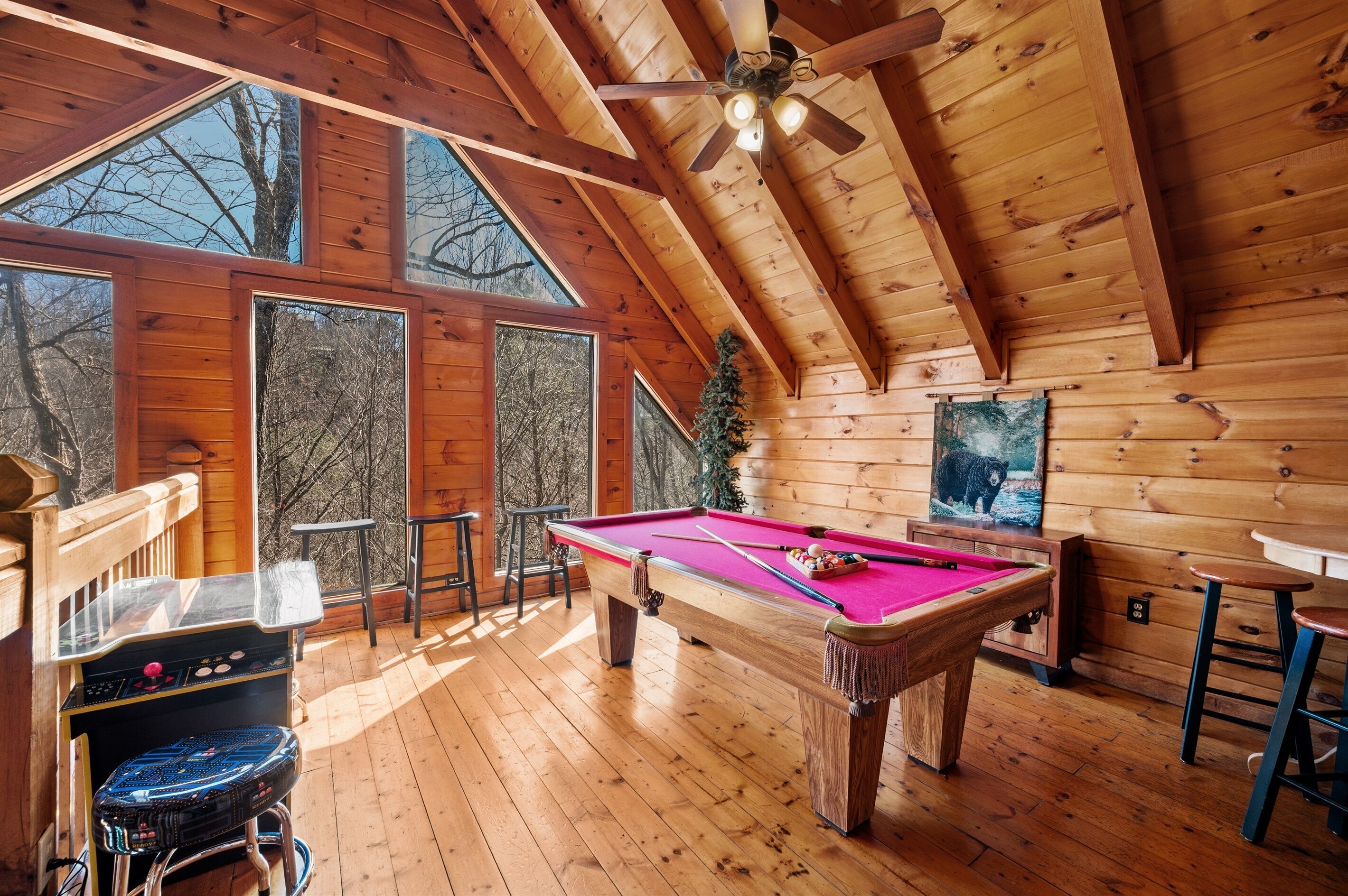 A wooden interior with a pool table, a ceiling fan, and large windows.