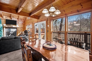 L’intérieur d’un chalet en bois comprend un coin repas, une cheminée et de grandes fenêtres donnant sur une terrasse.