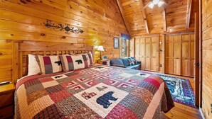 Ein Schlafzimmer in einer Blockhütte mit einem großen Bett, Holzwänden, einem Deckenventilator und einer Decke mit Tiermotiven.