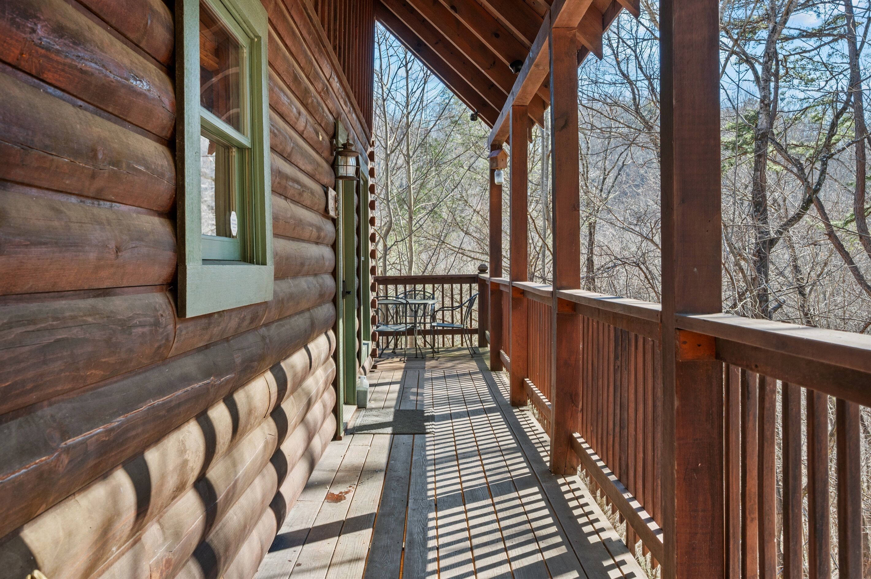A wooden log cabin with a covered porch and a view of the surrounding forest.