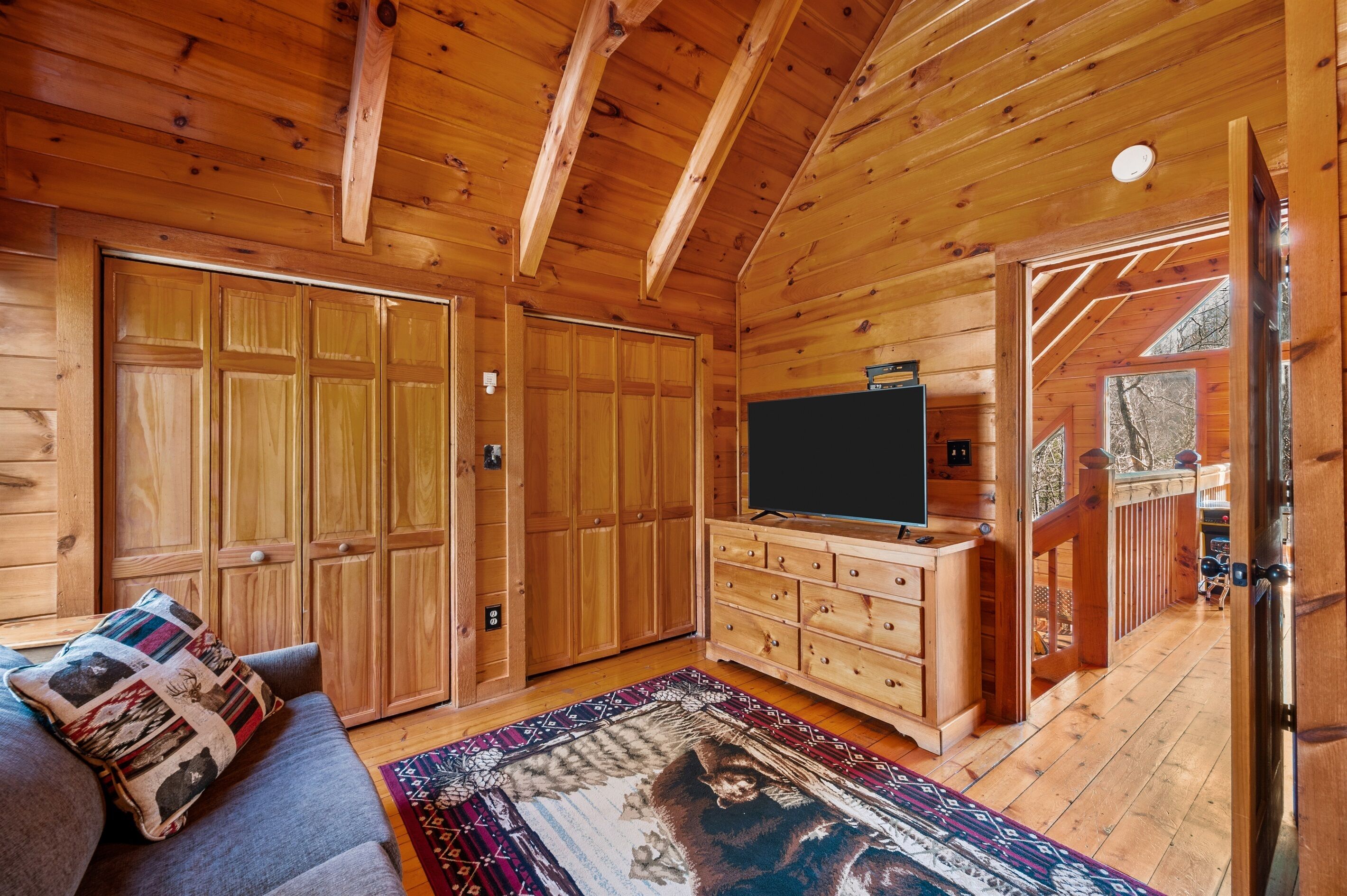 A log cabin interior with a sofa, a TV, a wooden dresser, and a large window.