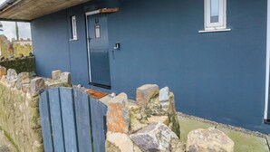 A house with a dark blue exterior, a wooden roof, a stone wall, and a blue door. - Red Kite Cottage (Haverfordwest)