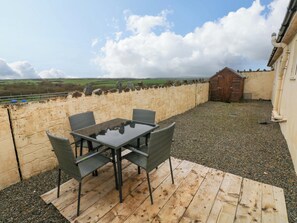 Un patio con mesa y sillas, una terraza de madera, un muro de piedra y vistas al campo.