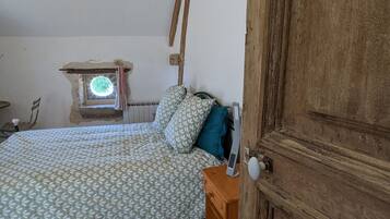 Une chambre à coucher avec un lit, une table de chevet en bois, une porte en bois et une petite fenêtre donnant sur un paysage verdoyant.