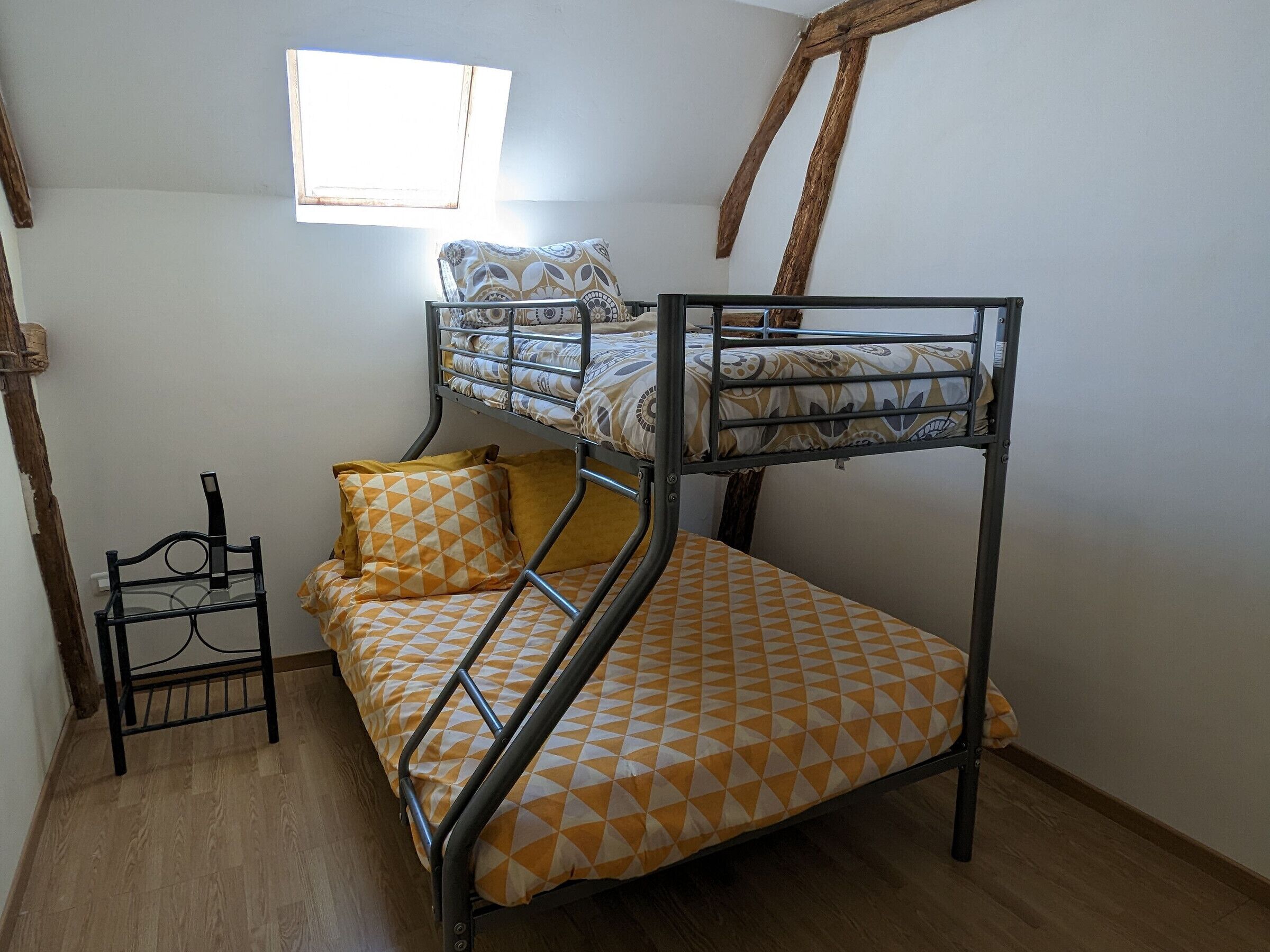 A bunk bed with patterned bedding, a small chair, and a window with natural light.