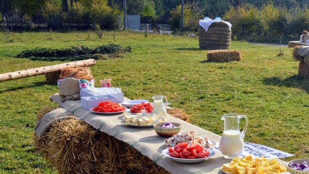 Een picknickopstelling met hooirollen, een tafel met eten en een landelijk landschap op de achtergrond.