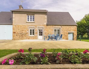 A two-story stone house with a front door, a small window, and a patio with blue chairs. - Countryside house in Normandy - 6 guests (Chérencé-le-Héron)