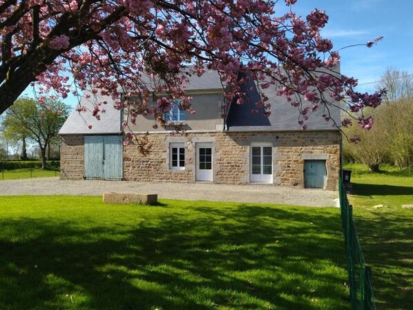 A two-story stone house with a grassy yard and a tree with pink blossoms in front. - Countryside house in Normandy - 6 guests (Chérencé-le-Héron)