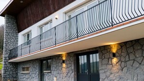 A modern building with a stone facade, a balcony with a unique railing design, and exterior lighting. - Mid-Century Stay in Val-d'Ajol with Parking and Pets Welcome (Le Val-d'Ajol)