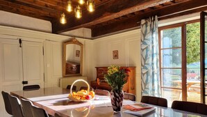 Comedor con mesa de madera, sillas, un florero con flores y vistas al exterior a través de una ventana.