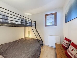 Ein Stockbett mit einer Stehle, ein kleiner Tisch, eine Heizung und ein Fenster mit Blick auf ein Gebäude.