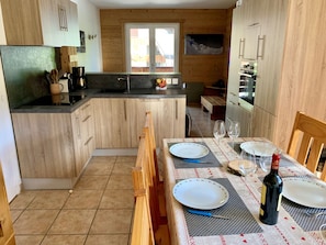 A kitchen with wooden cabinets, a dining table set with plates, glasses, and a bottle of wine. - Cozy apartment - 6 guests (Les Gets)
