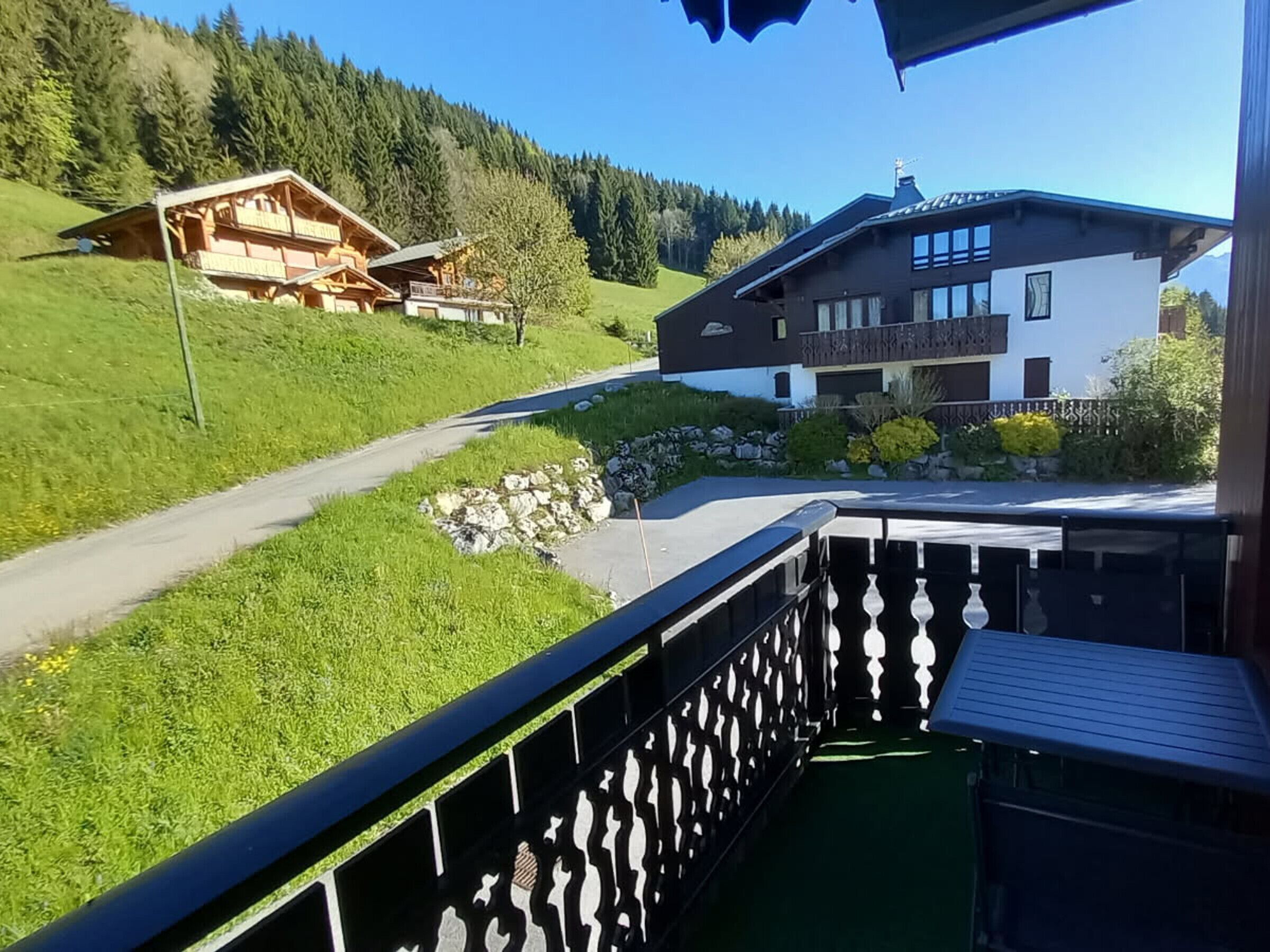 A balcony with a view of a mountain road, a wooden chalet, and a modern house with a balcony.