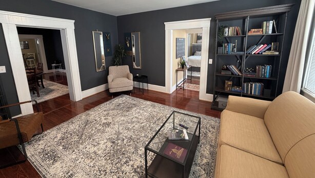 A living room with a dark wall, a beige sofa, a coffee table, a bookshelf, and a dining area visible through an open door. - A stylish and quiet, comfortable space with full house accommodations (Chillicothe)