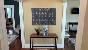 A hallway with a wooden floor, a patterned rug, a table with a book and a plant, and a wall-mounted phonetic alphabet chart. - A stylish and quiet, comfortable space with full house accommodations (Chillicothe)