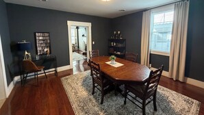 A dining area with a wooden table and chairs, a rug, a bookshelf, and a window with curtains. - A stylish and quiet, comfortable space with full house accommodations (Chillicothe)