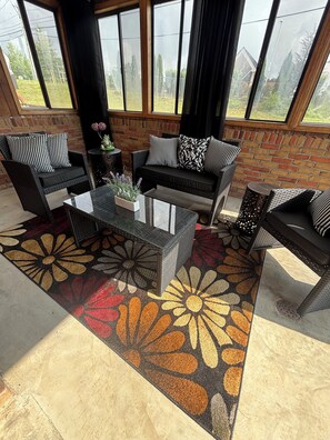 A sunlit patio with a brick wall, a glass coffee table, and two sofas with striped cushions.