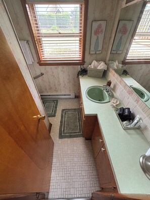 A compact bathroom with two sinks, a window with blinds, a towel rack, and a small plant.