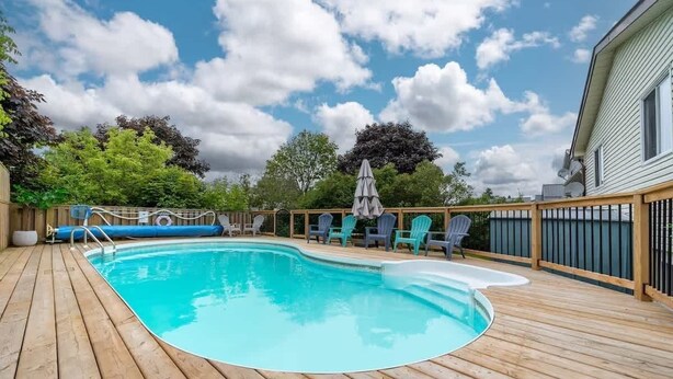 Una terraza de madera con piscina, rodeada por una valla y árboles.