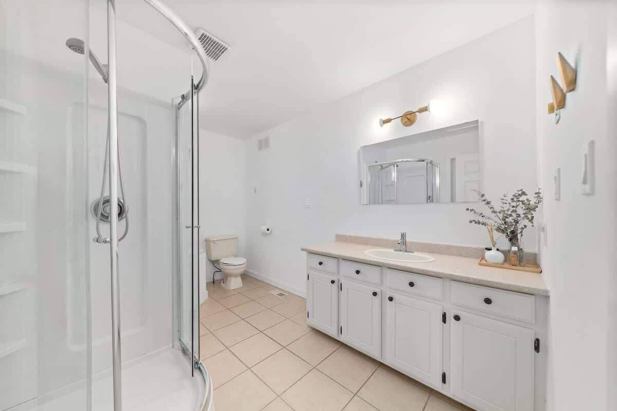 Un baño moderno con cabina de ducha de vidrio, inodoro blanco y tocador con espejo y lavamanos.